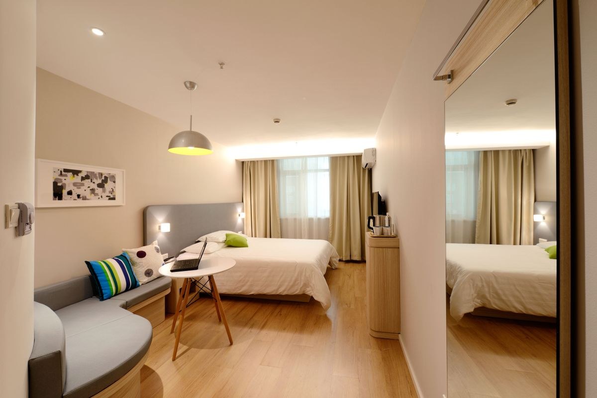 Compact bedroom with a double bed, a built-in grey sofa with cushions and a mirrored wall